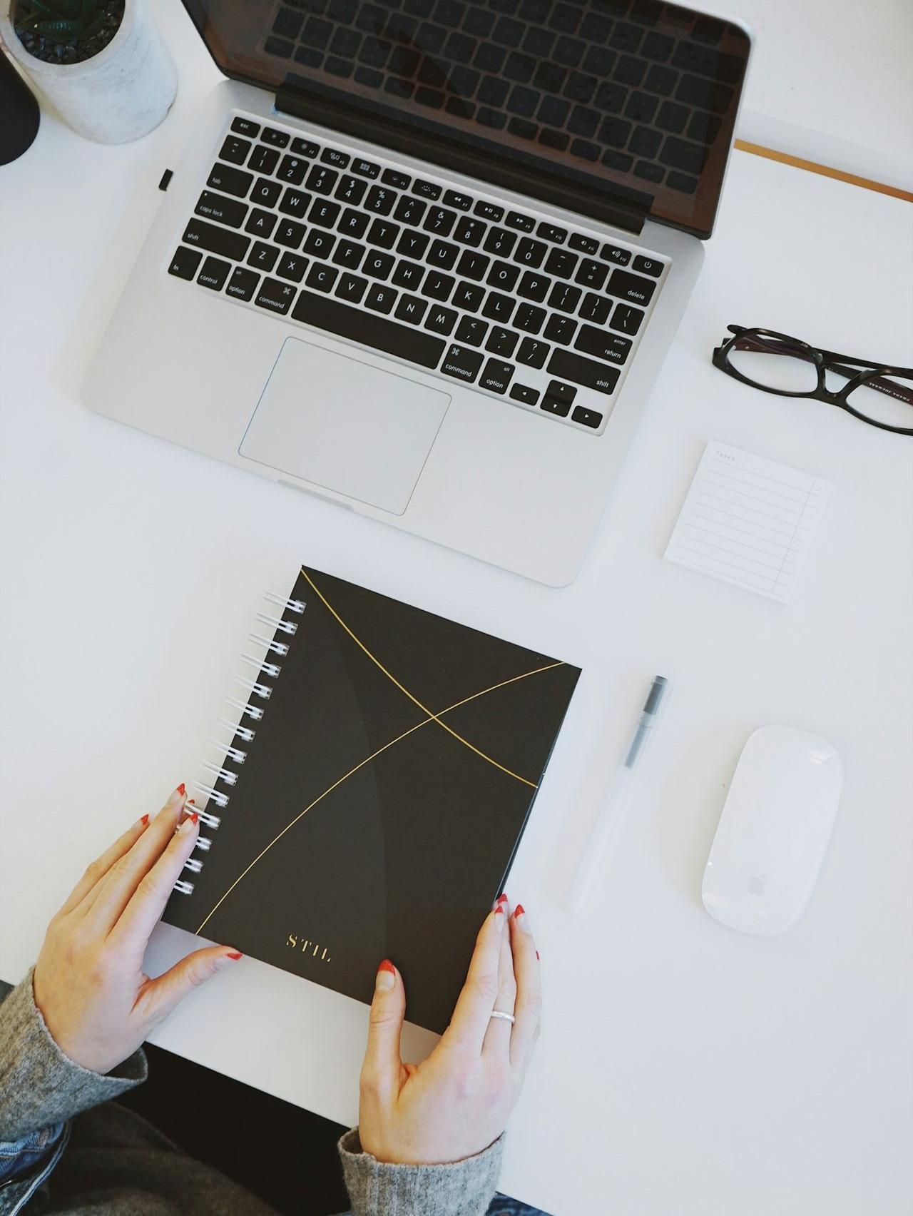 person holding notebook near laptop